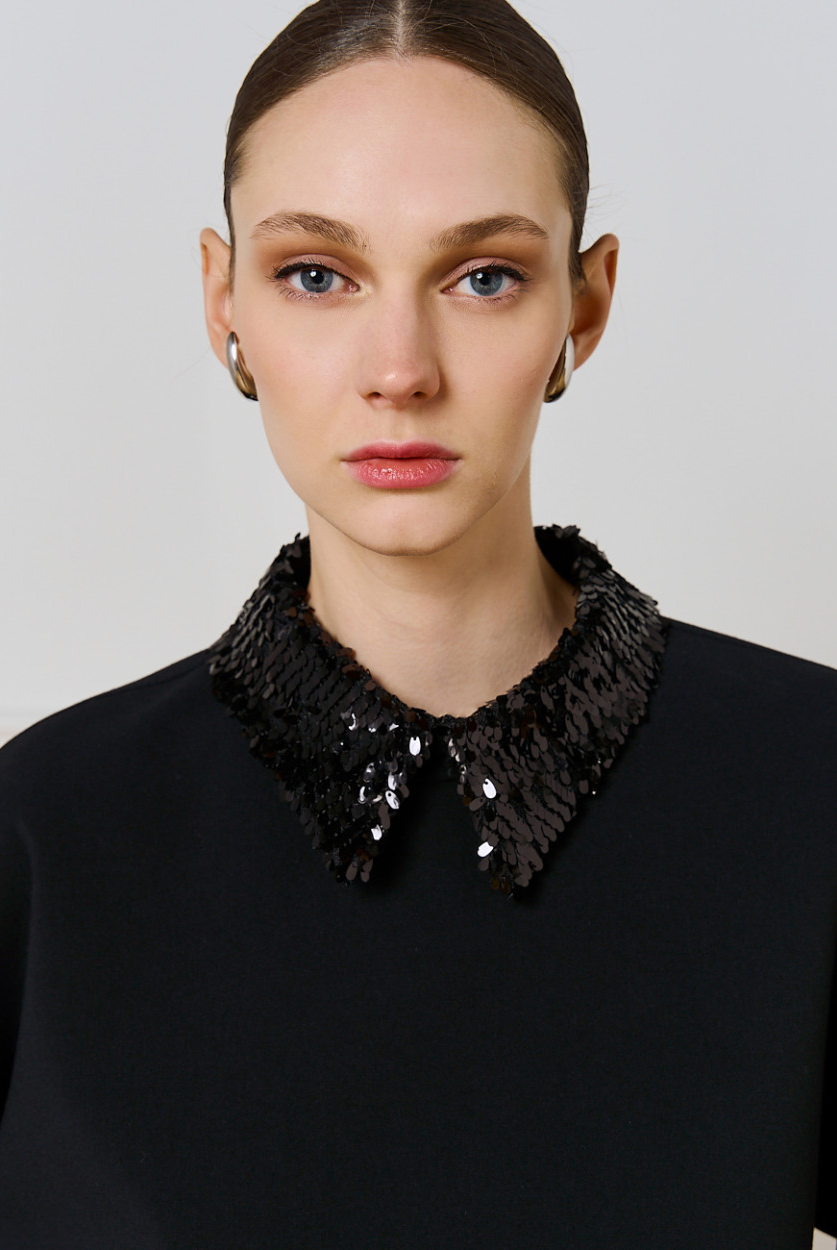 Close-up of Access Fashion black detachable sequin collar on black top, worn by model.