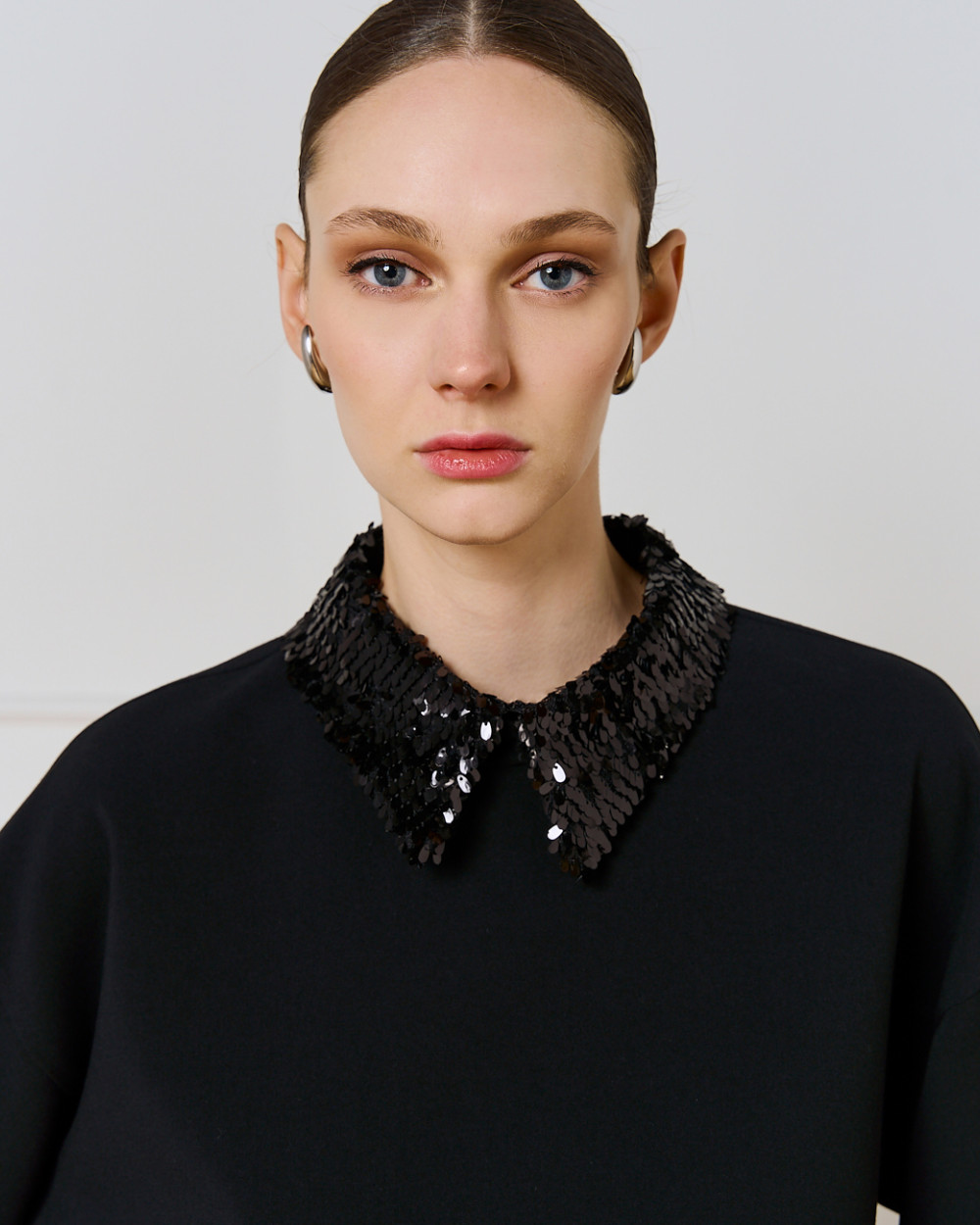 Close-up of Access Fashion black detachable sequin collar on black top, worn by model.