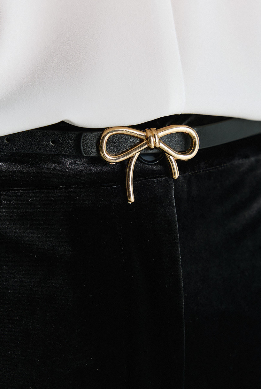 Access Fashion thin black faux leather belt with gold bow buckle close up.