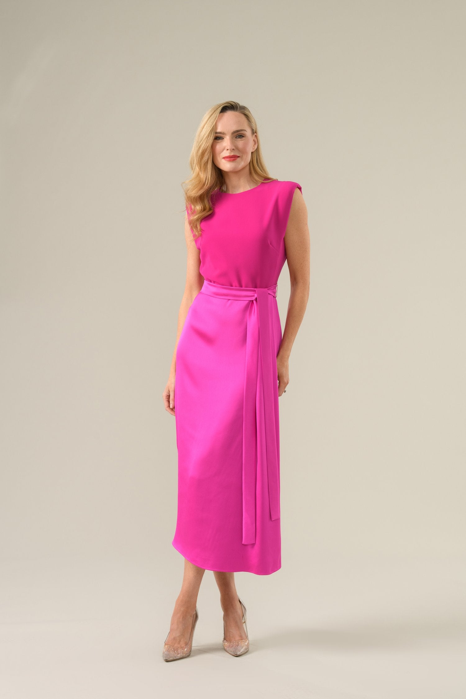 Woman wearing a bright pink occasion dress from Caroline Kilkenny on a beige background