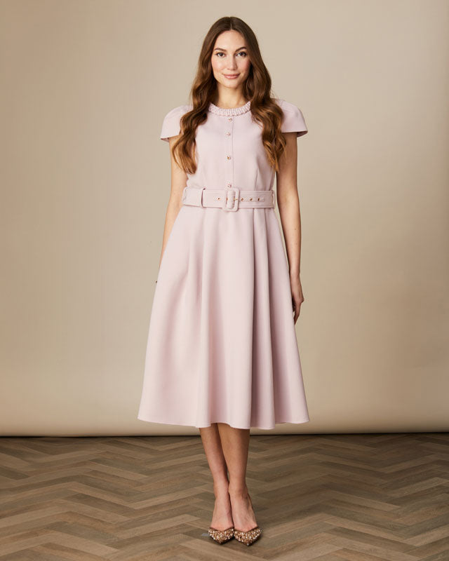 Model wearing light pink Fee G Charlotte dress with short sleeves and pleated skirt.