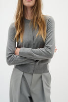 Cropped close-up of model crossing arms in soft grey cardigan and trousers