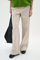 Close-up of beige bootcut trousers styled with green textured top and black tote