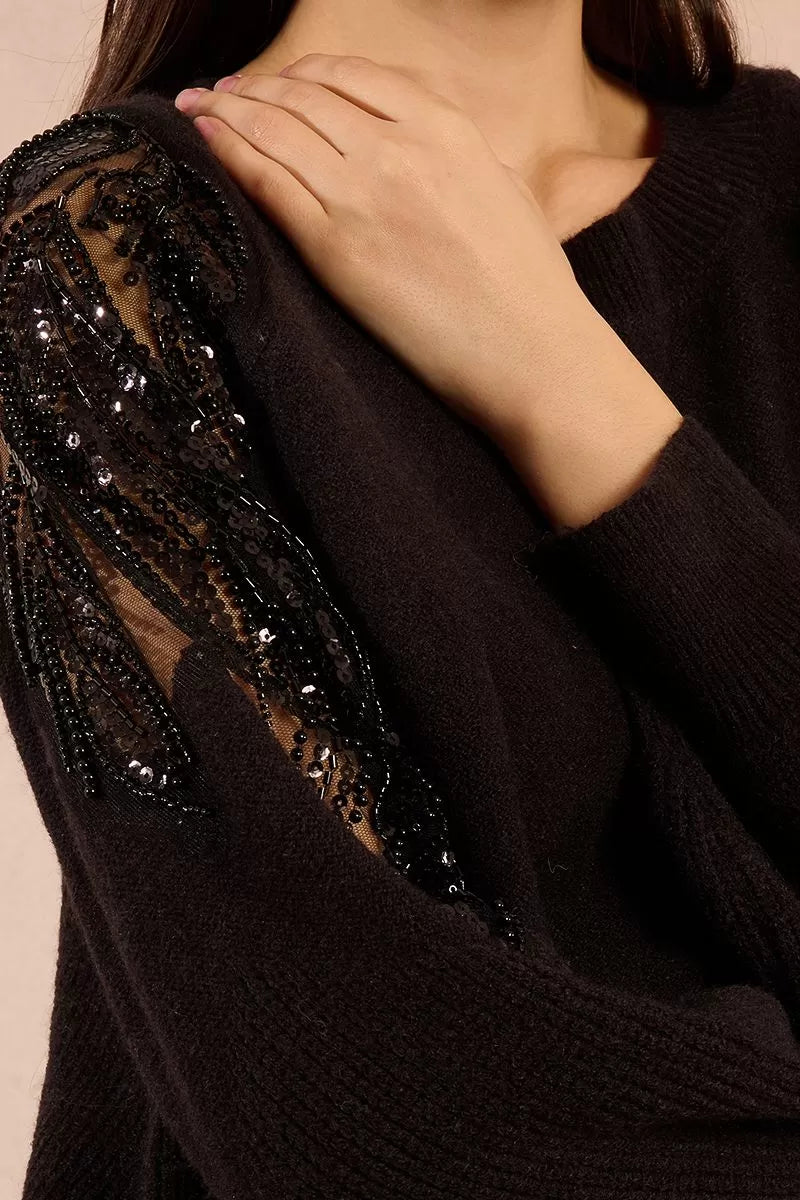 Close-up of black knit jumper with sheer lace sleeve and rhinestone detail