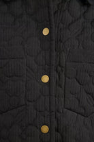 Close-up of floral stitched quilting and brass buttons on black jacket