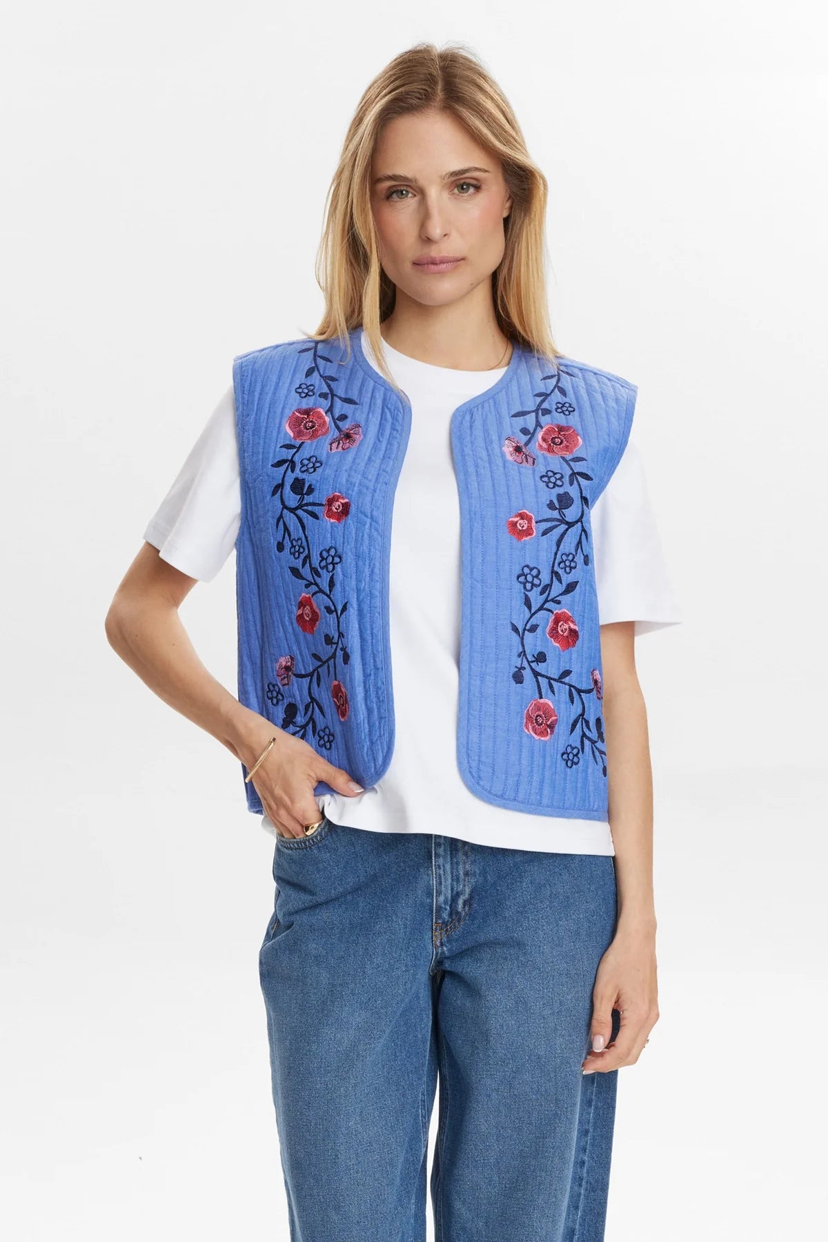 Model wearing Numph Nujodie blue quilted gilet with red floral embroidery