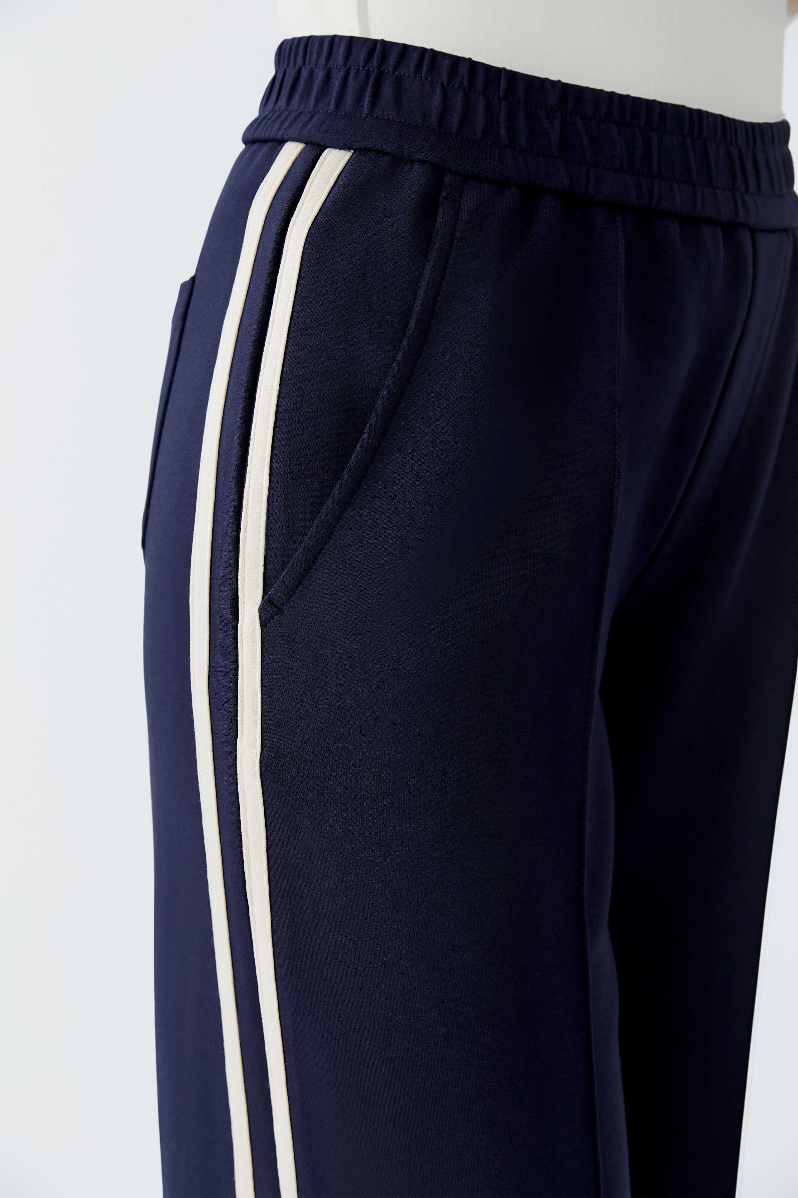 Detailed side angle of cream striped trim and structured waistband on navy trousers