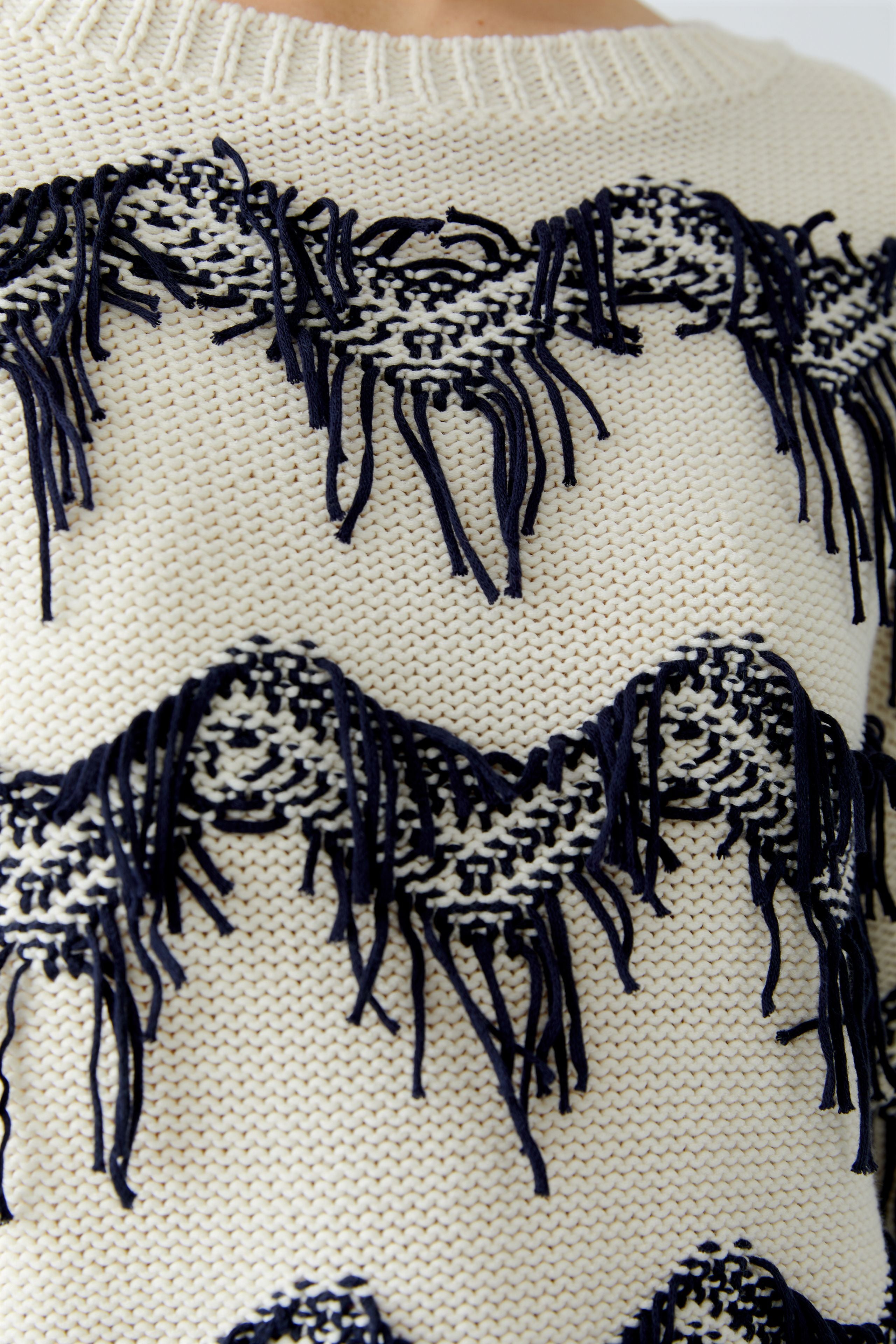Close-up of a sweater with funky fringe designs and fringes.