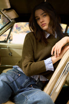 Model seated in car wearing Oui striped blouse layered under olive knit jumper