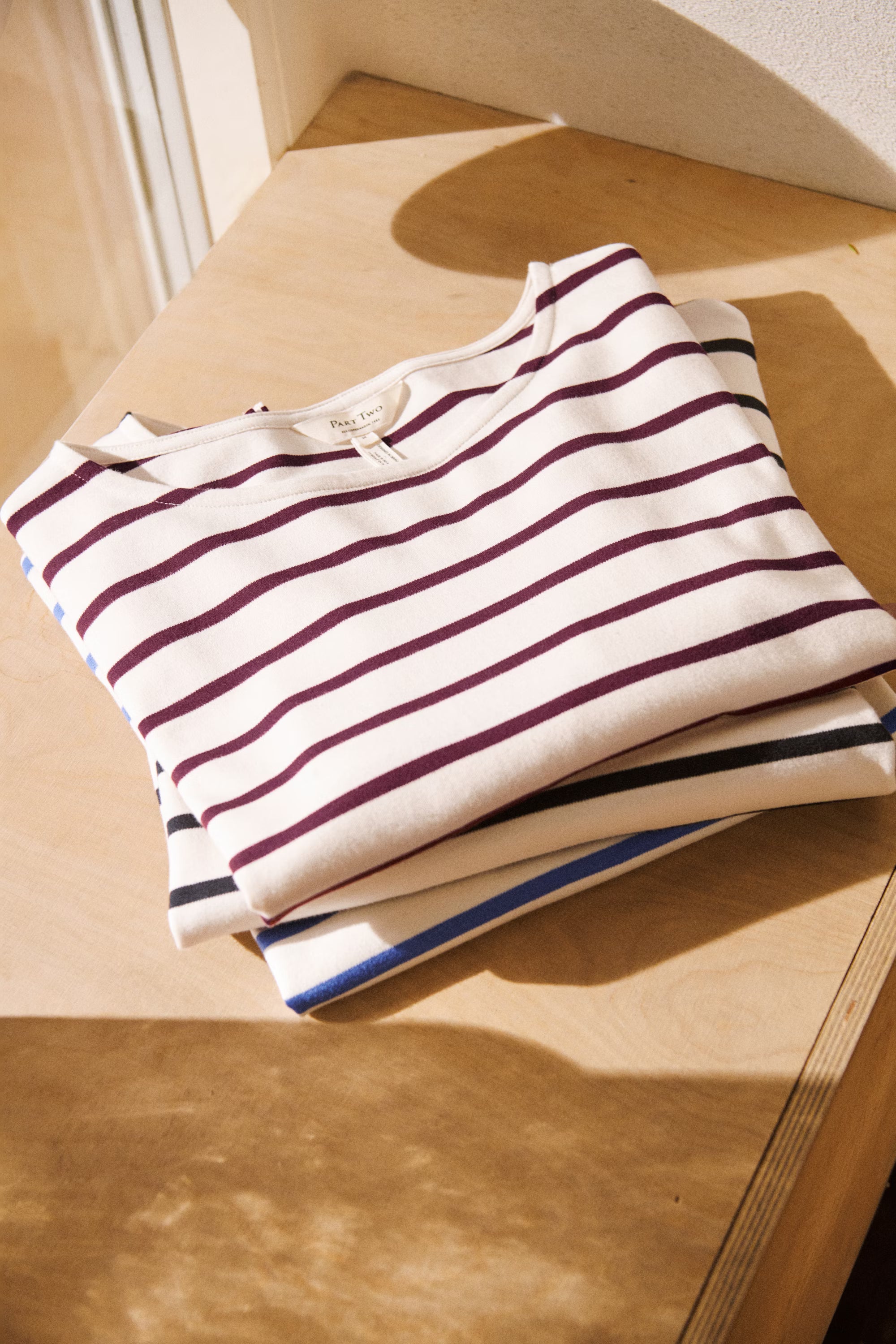 Folded Part Two NelaPW striped top in cream with burgundy stripes, displayed on a wooden surface.