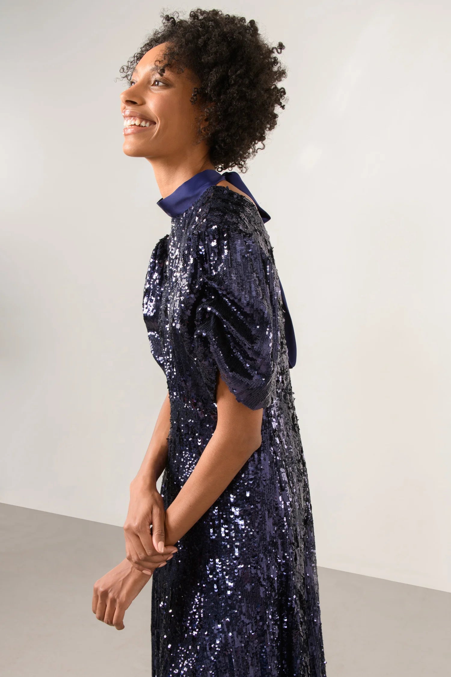 Side view of model in navy sequin dress with gathered waist and high neckline