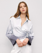 Model wearing grey gradient satin wrap shirt styled with white trousers