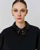 Close-up of Access Fashion black detachable sequin collar on black top, worn by model.