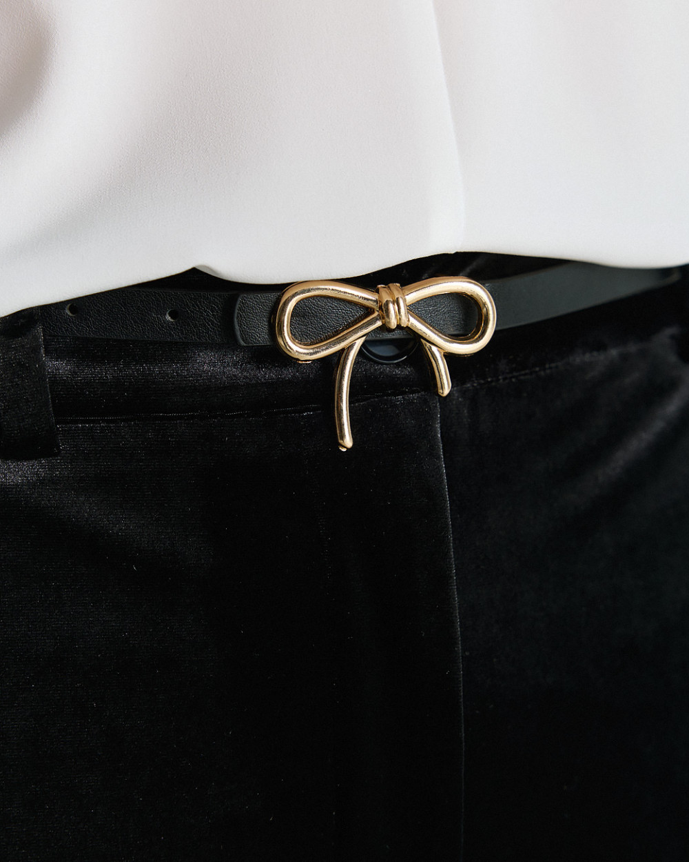 Access Fashion thin black faux leather belt with gold bow buckle close up.