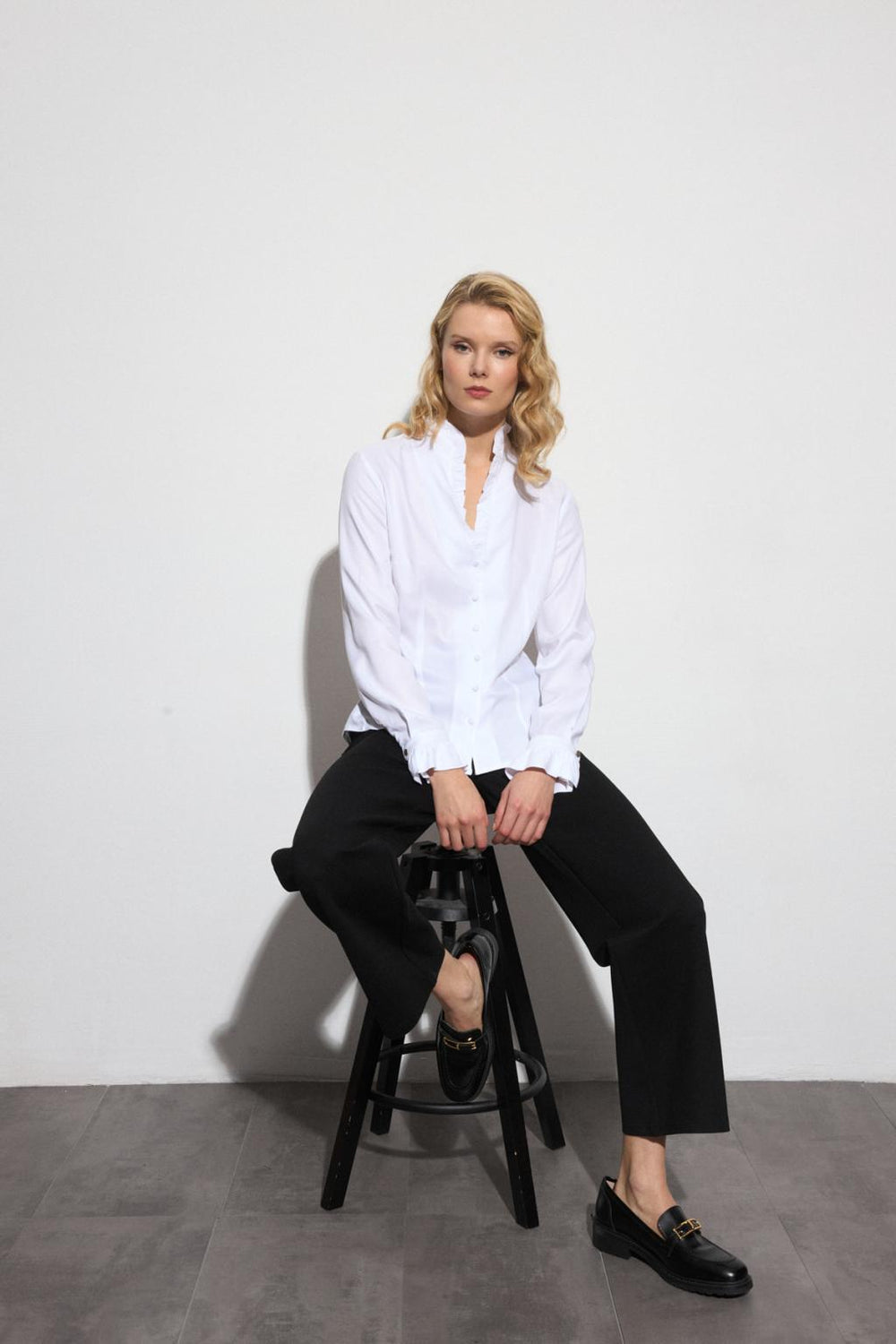 Bariloche white ruffle shirt styled seated with monochrome look
