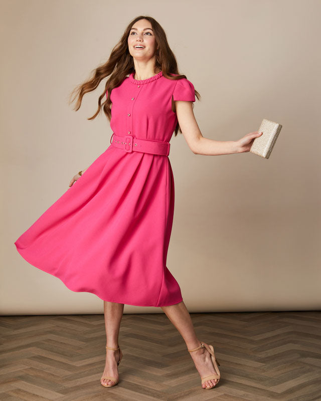 Model wearing pink Charlotte swing dress with short sleeves and pleated skirt.