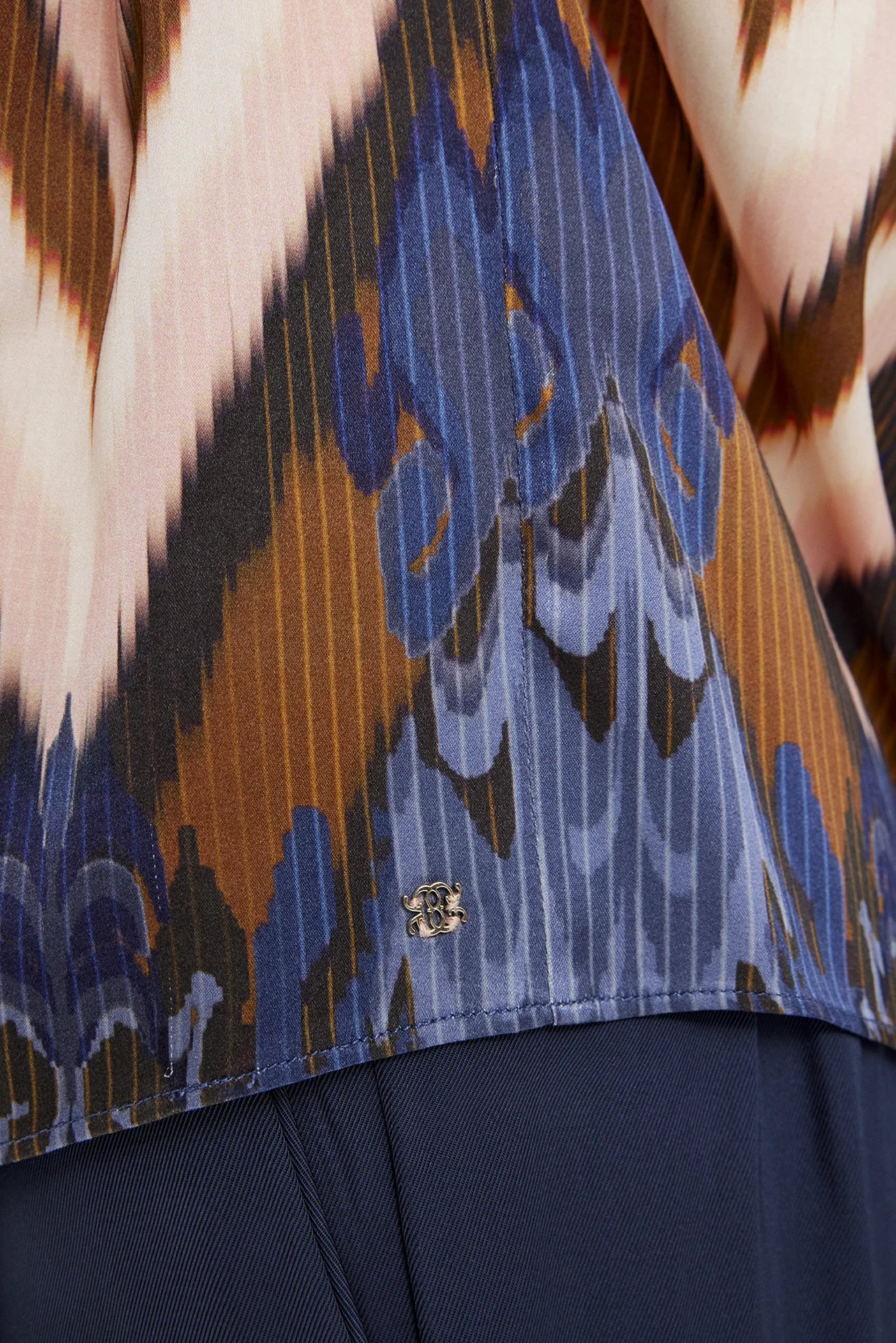 Close-up of pleated zig zag fabric and floral hem detail on Gustav silka blouse