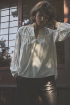 Gustav Annsofie off-white pleated blouse worn with dark trousers, showing front neckline and gathered detailing.
