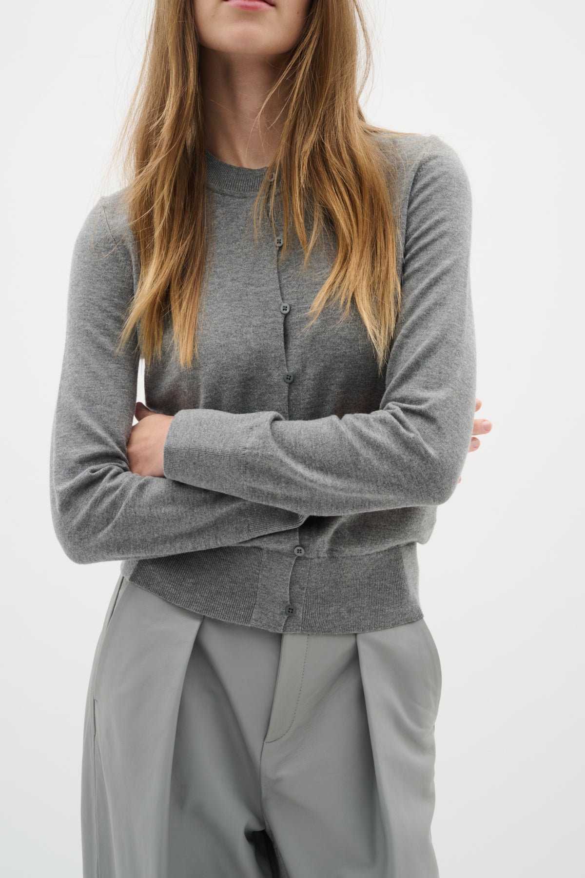 Cropped close-up of model crossing arms in soft grey cardigan and trousers
