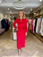 Woman wearing Kameya red belted slit neckline dress in boutique, styled with nude heels