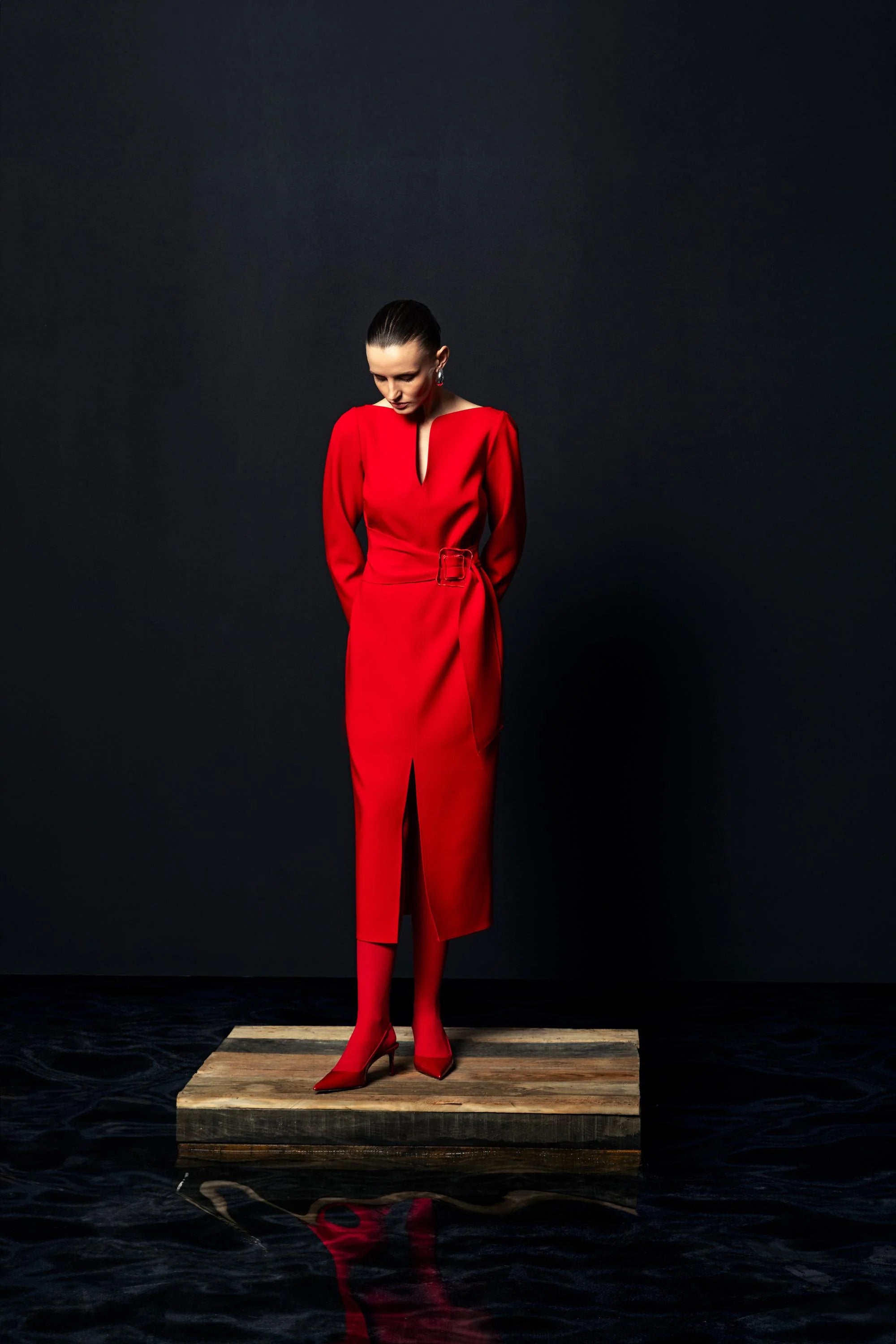 Model in Kameya red belted dress with long sleeves and front split, standing on platform
