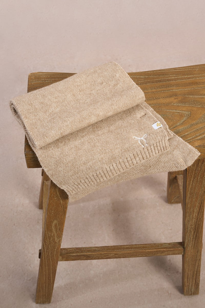 Close-up of Molly Bracken beige scarf showing stitched bow and clover tag