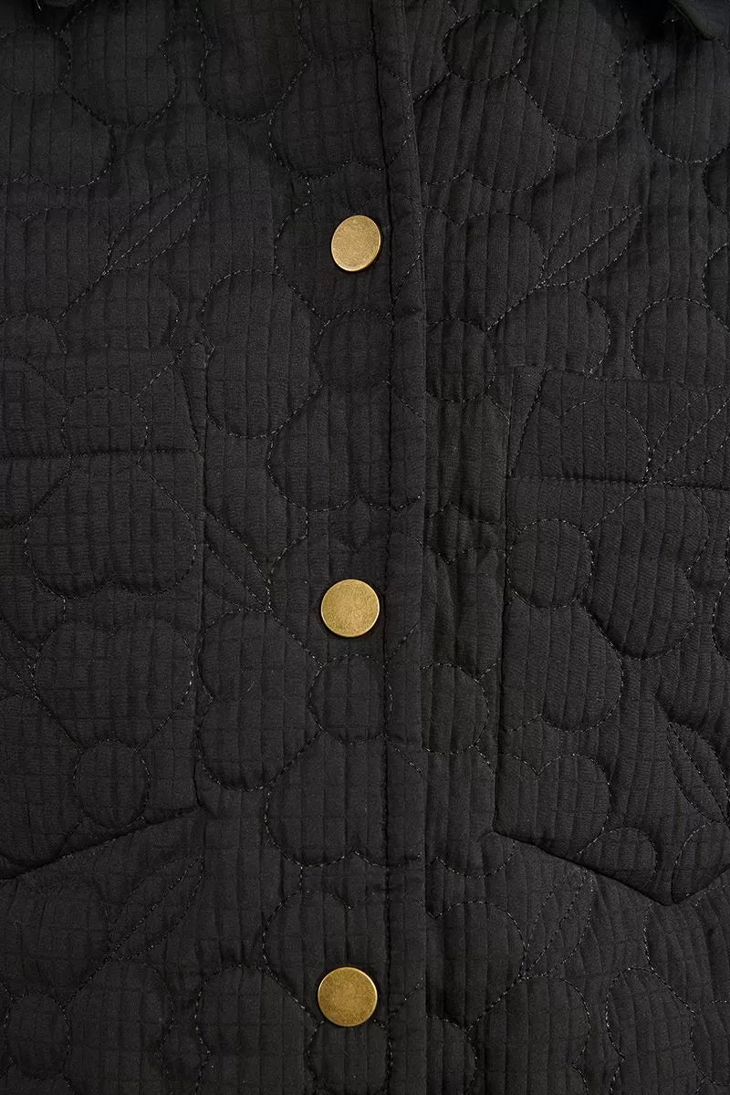 Close-up of floral stitched quilting and brass buttons on black jacket