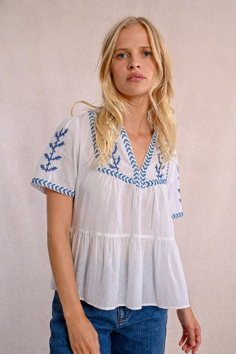 Model wearing white embroidered summer  V-neck top with short sleeves and blue accents.