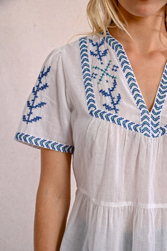 Detail shot of blue embroidery on white cotton blouse sleeve and neckline.