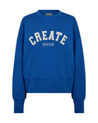 Model wearing Mos Mosh Celi Create cobalt-blue sweatshirt with slogan