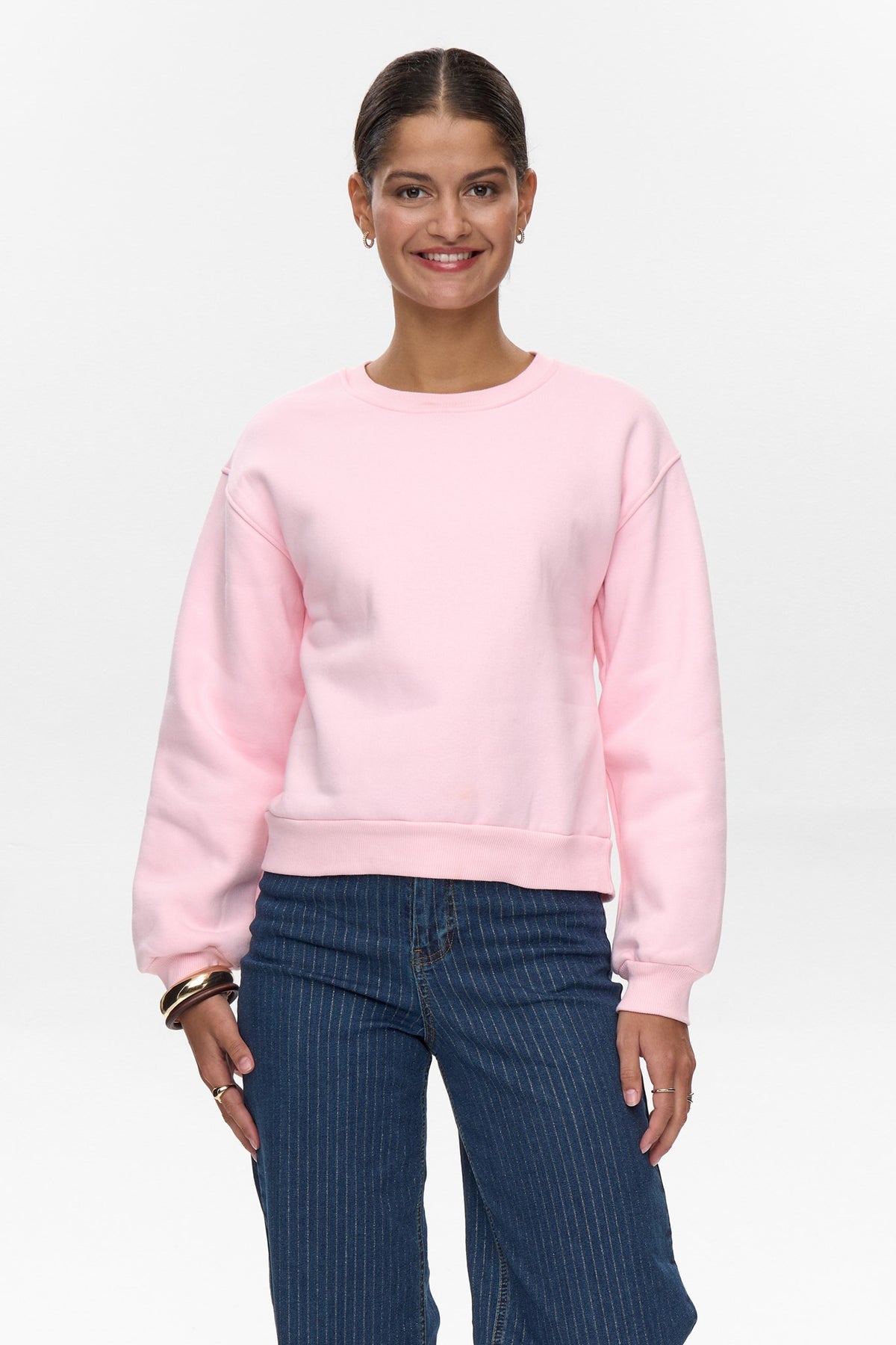 Front view of model wearing Numph cherry blossom pink crew neck sweater with relaxed fit and blue jeans