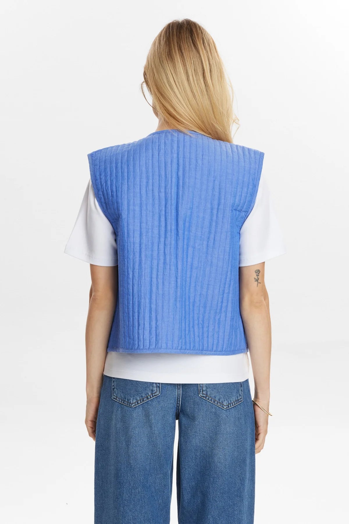 Person wearing a blue vest over a white shirt with blue jeans on a light gray background