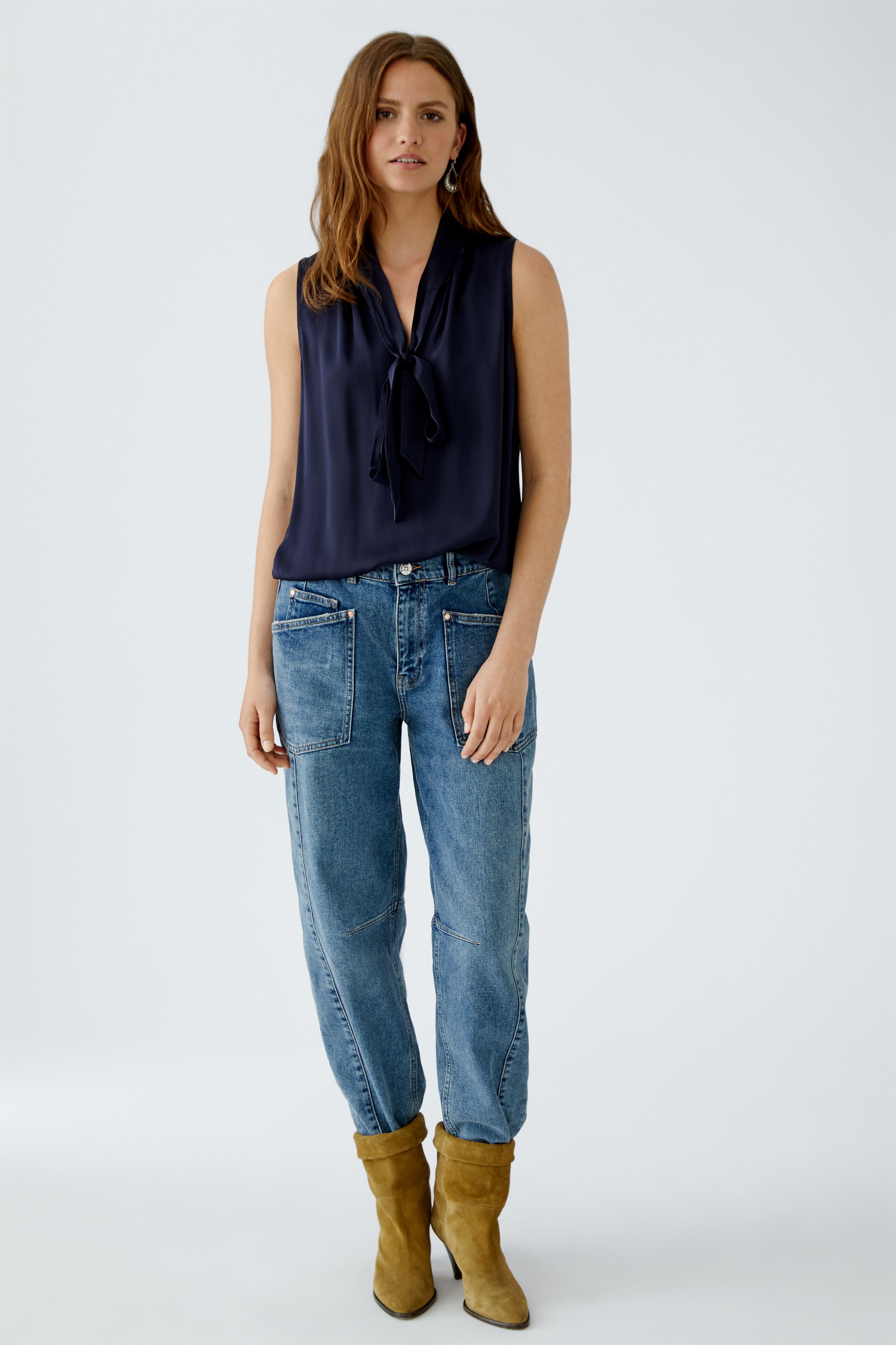 Full-body front view of model wearing navy satin Oui blouse with bow neck and jeans