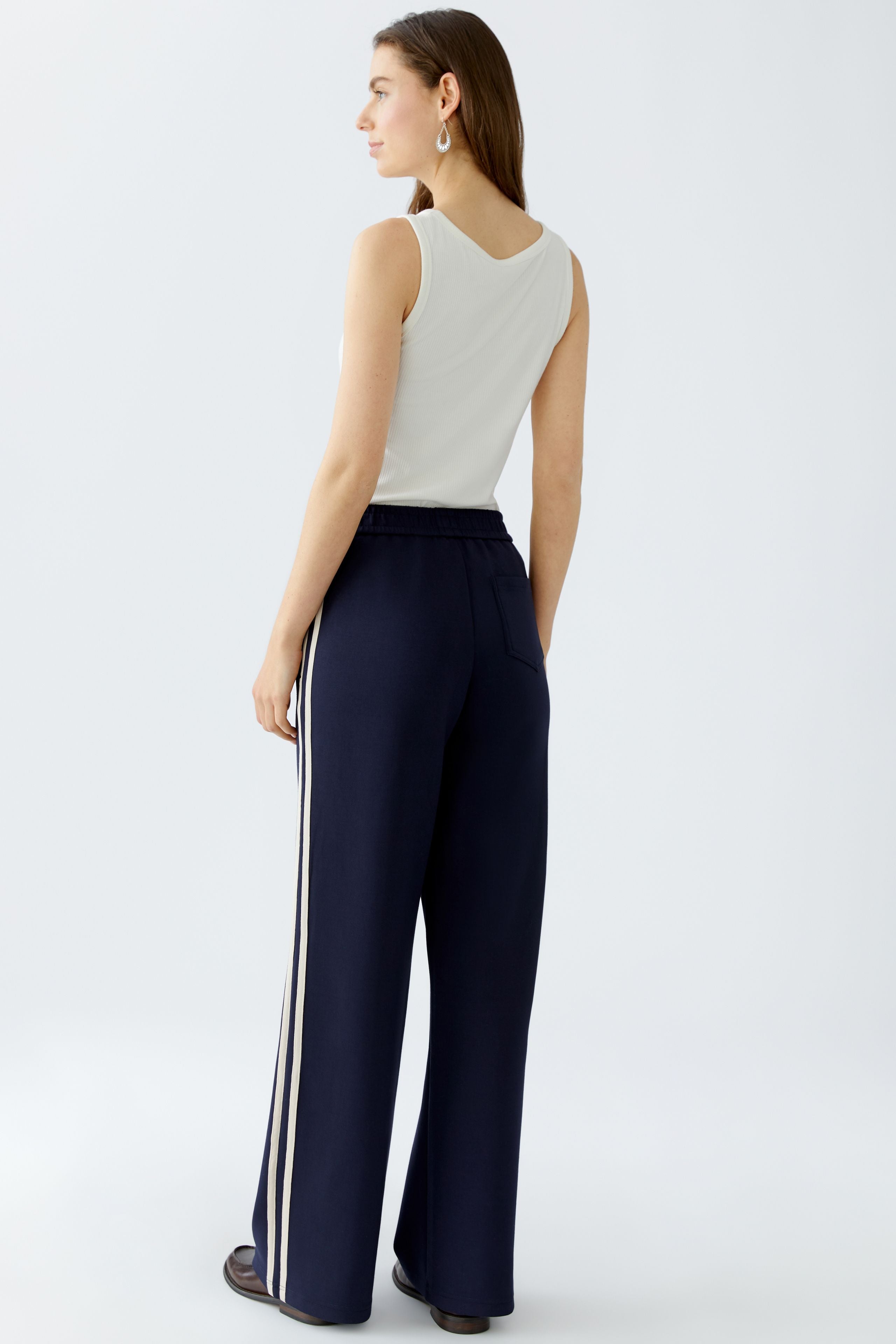 Model wearing wide-leg navy slip-on trousers with relaxed cream vest top, back view