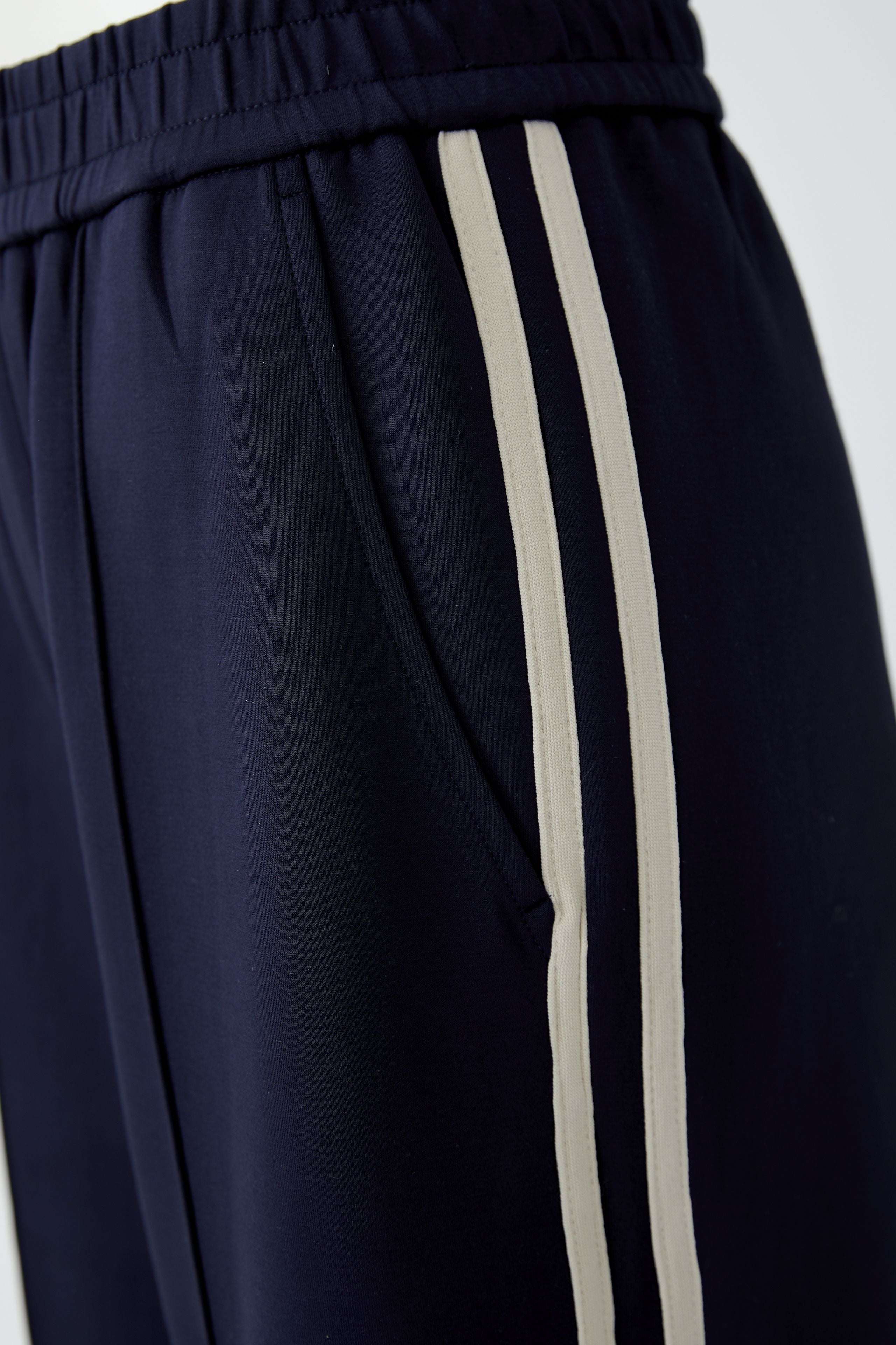 Close-up of elasticated waistband and cream contrast stripes on Oui navy trousers
