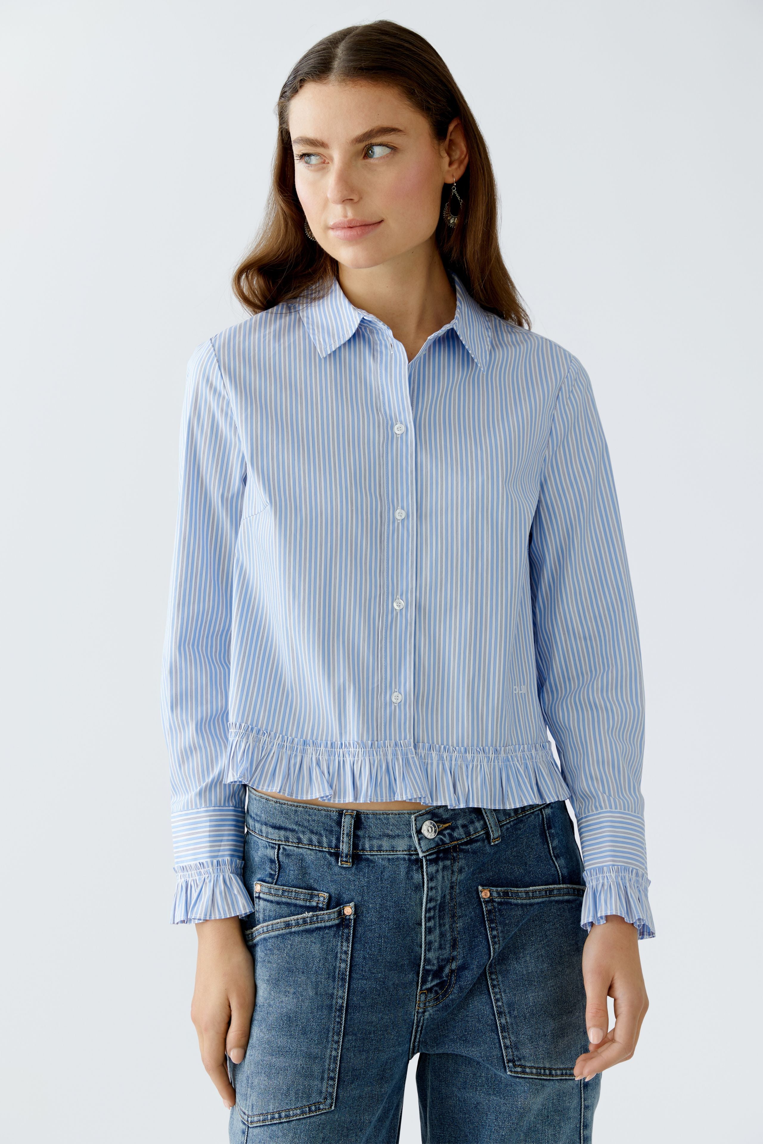 Model standing facing forward in blue and white ruffle blouse and casual jeans