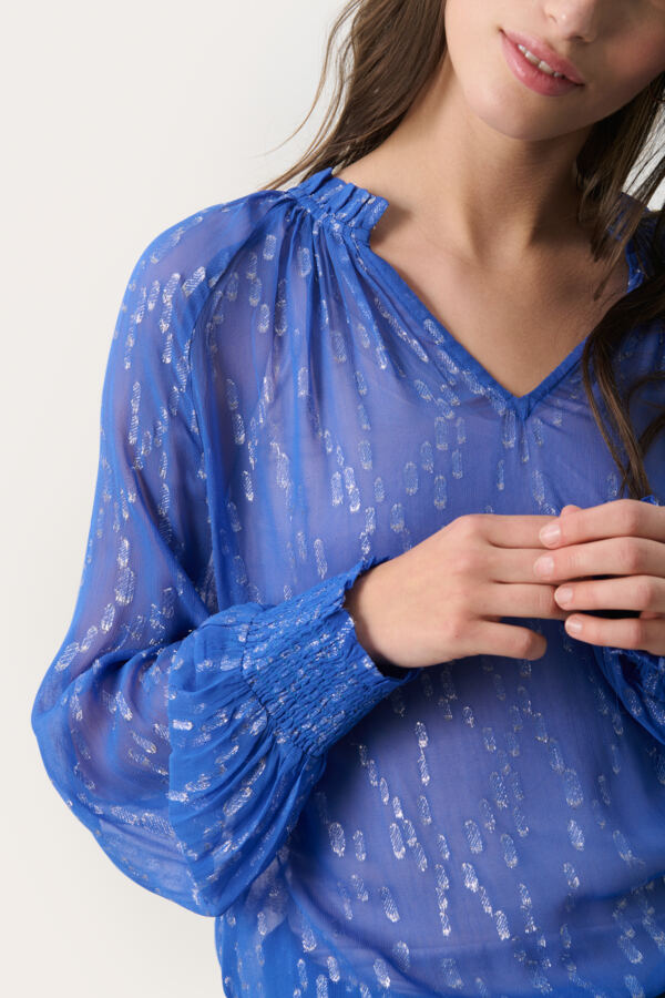 Close-up of sparkly blue lurex blouse with soft V neckline and gathered cuffs