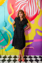 Sisters Milo black cotton tiered shirt dress styled against colourful mural