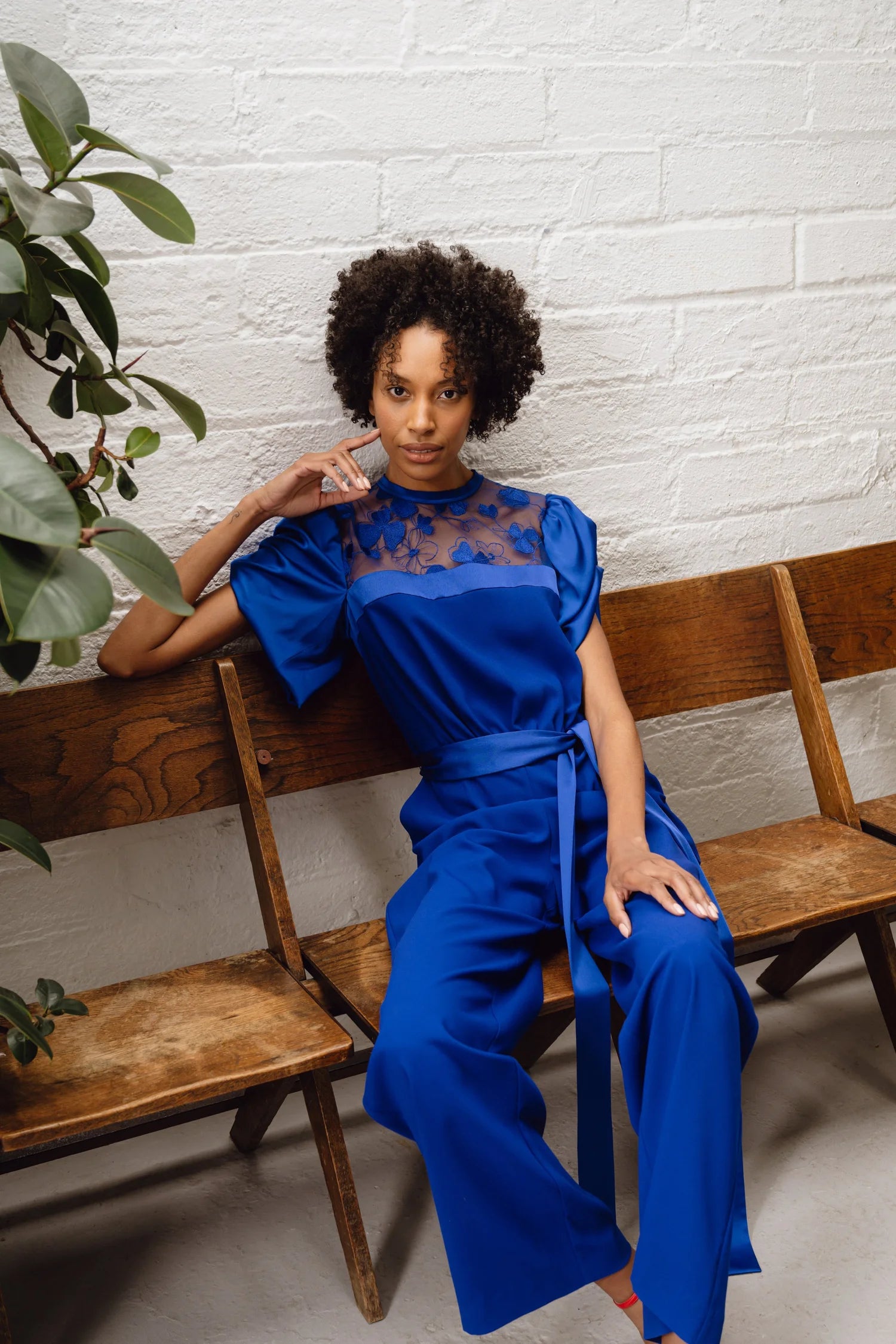 Samantha jumpsuit full-length seated pose on wooden bench, self-tie belt visible