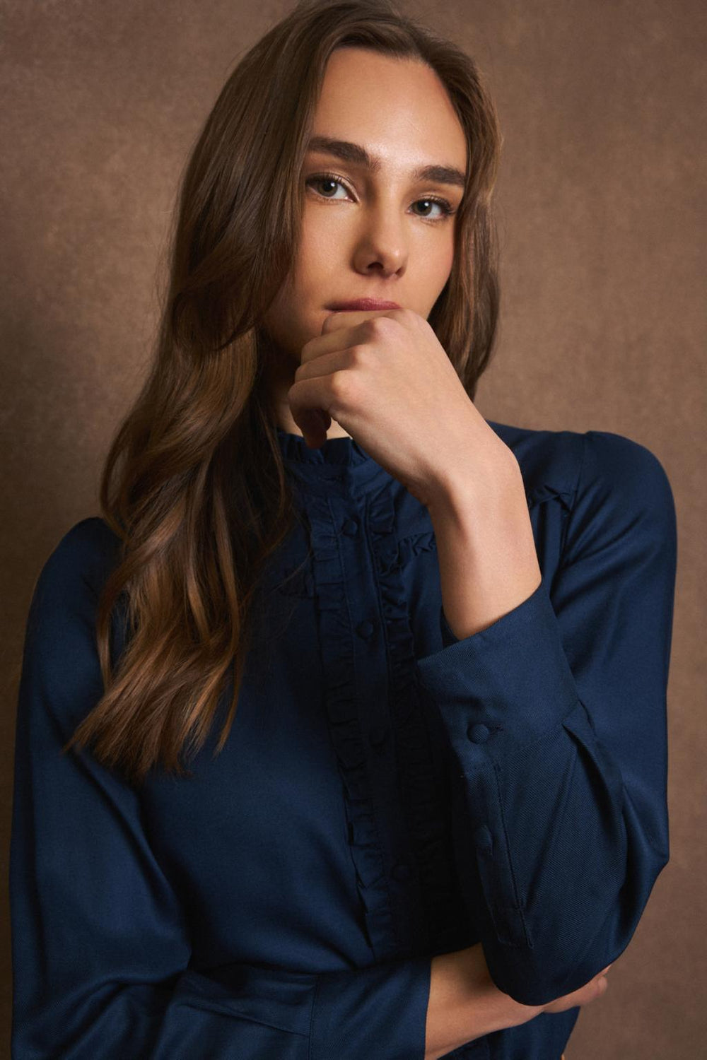 Model in navy shirt with hand to face and subtle ruffle detail